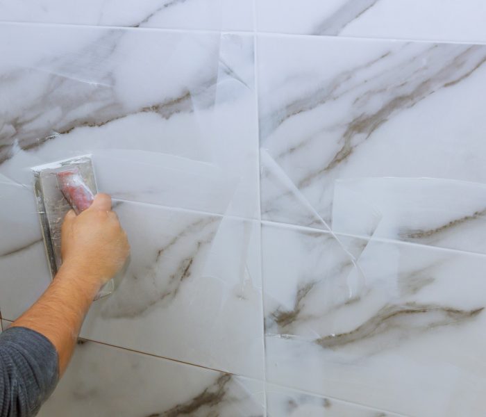 Grouting tiles male hand with the rubber applies grout on a seam between tiles