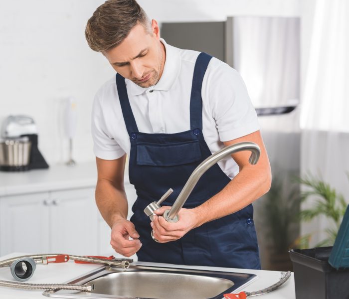 thoughtful adult repairman taking off kitchen faucet for repairing